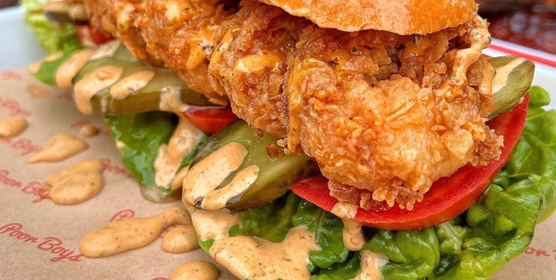 Fried chicken sandwich topped with fresh lettuce and tomatoes, served on a toasted bun.