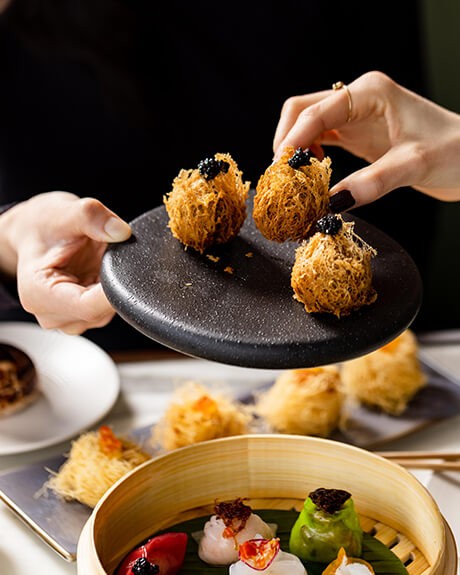 A person selecting a delicious dim sum from a black plate surrounded by a selection of other dim sum
