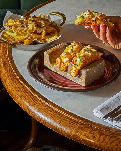 Delicious gourmet tacos served on a stone plate, accompanied by a side of truffle fries on a wooden table.