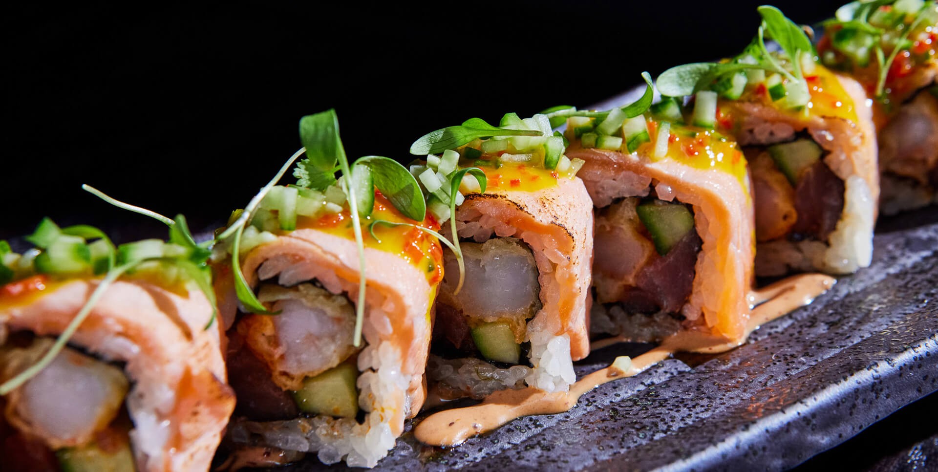 A row of exquisite sushi garnished with herbs and plated with a creamy dipping sauce